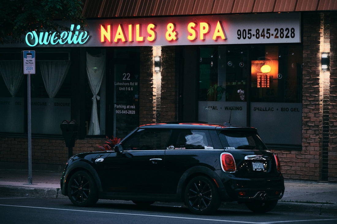 A black car parks in front of a nail salon.