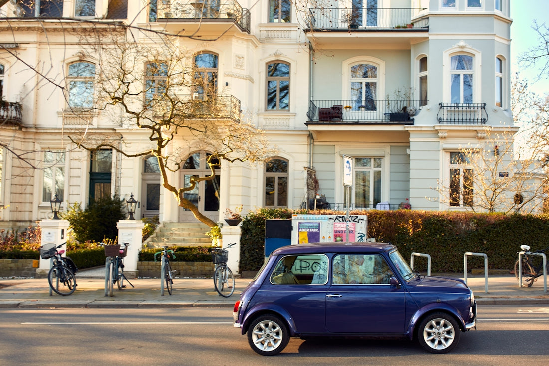 A blue mini cooper drives past ornate buildings.