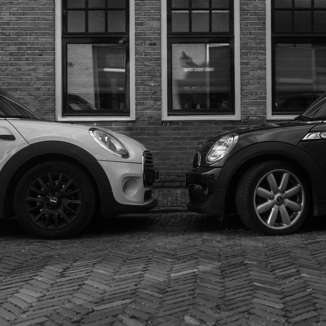 Two small cars parked facing each other on a brick street in front of windows