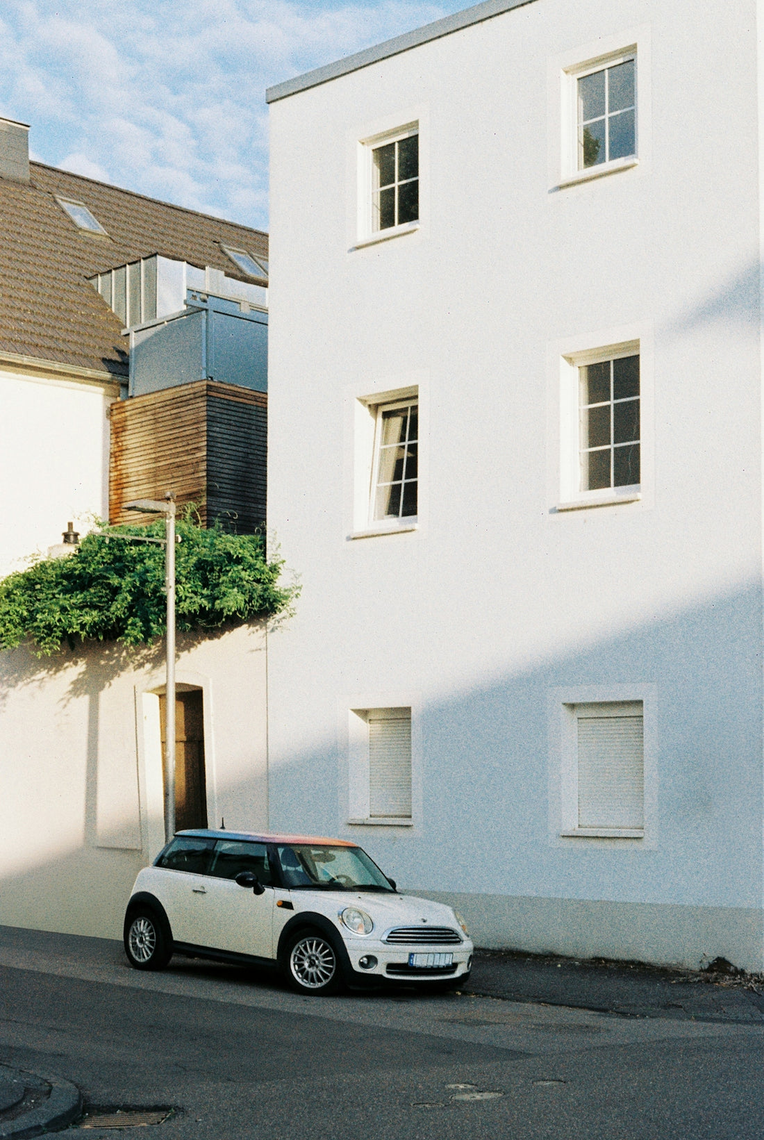 A white Mini Cooper parked on a street beside a tall white building